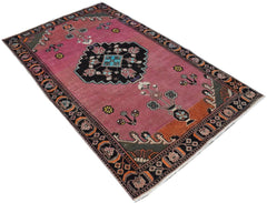 A handmade vintage Persian wool rug featuring a pink field with a central black medallion.