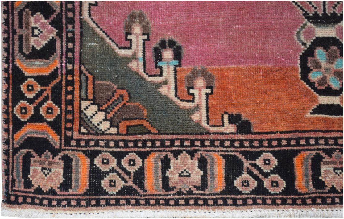 A close-up of a handmade vintage Persian rug featuring a geometric floral border and pink field.