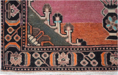 A close-up of a handmade vintage Persian rug featuring a geometric floral border and pink field.