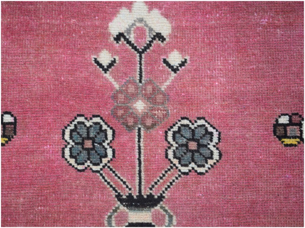 A vintage Persian rug featuring a stylized floral motif in shades of blue and pink on a rose background.