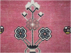 A vintage Persian rug featuring a stylized floral motif in shades of blue and pink on a rose background.