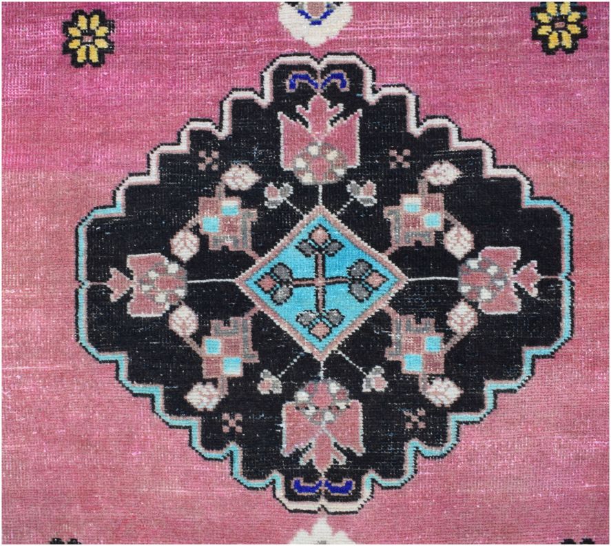 A vintage Persian rug featuring a central black geometric medallion with floral motifs on a pink field.