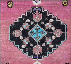 A vintage Persian rug featuring a central black geometric medallion with floral motifs on a pink field.