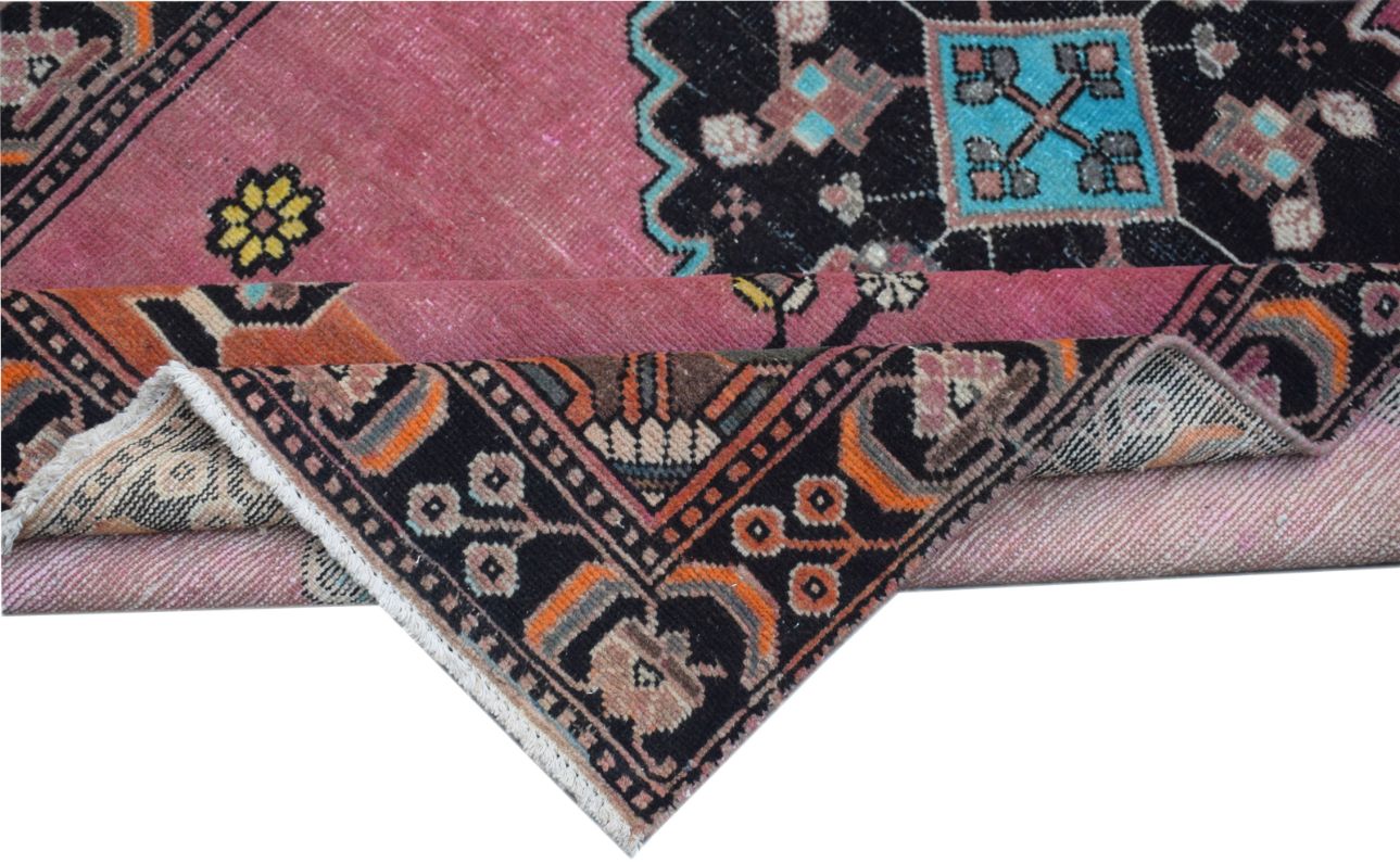 A vintage Persian rug with a pink field and black geometric borders folded to show the backing.