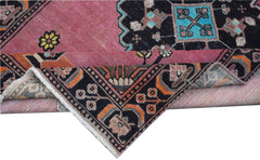 A vintage Persian rug with a pink field and black geometric borders folded to show the backing.