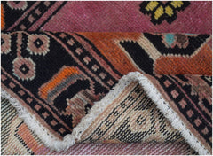 A folded vintage Persian wool rug featuring a geometric tribal pattern in pink, orange, and black.