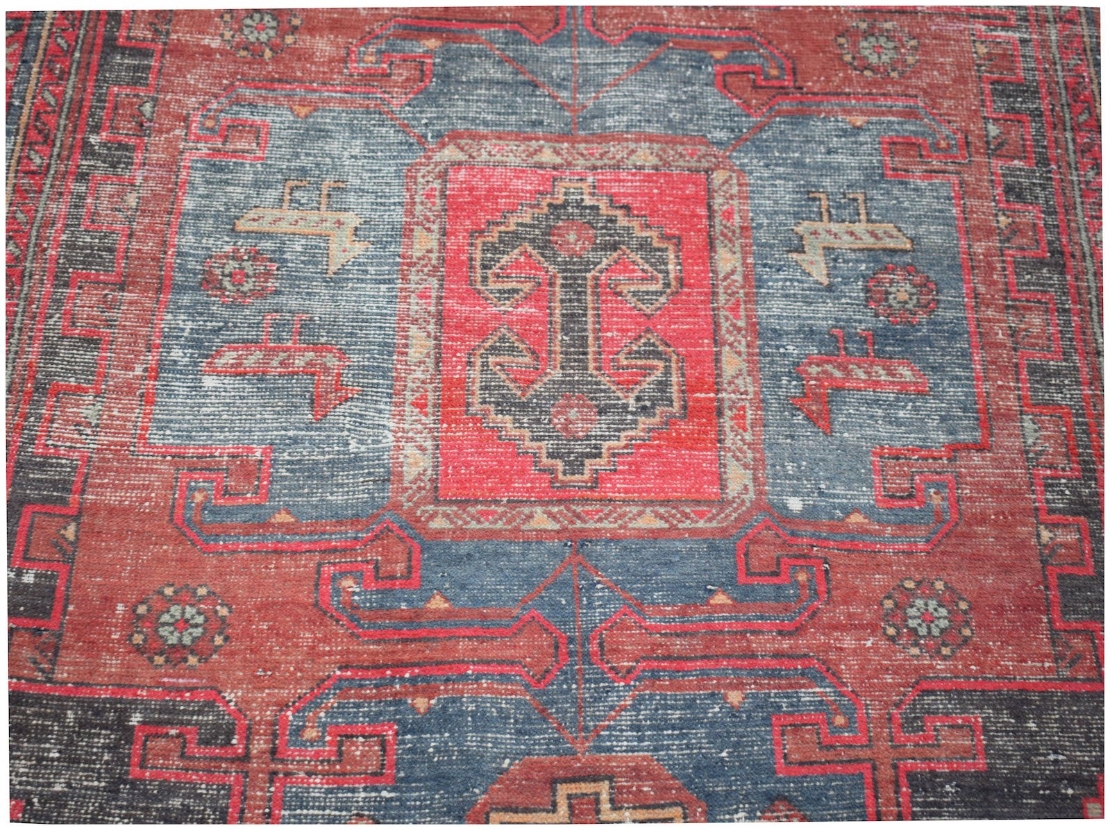 A vintage handwoven Persian rug featuring a geometric pattern in red, blue, and black wool.