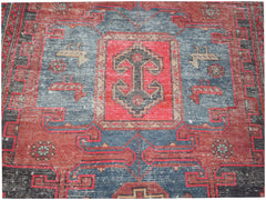 A vintage handwoven Persian rug featuring a geometric pattern in red, blue, and black wool.