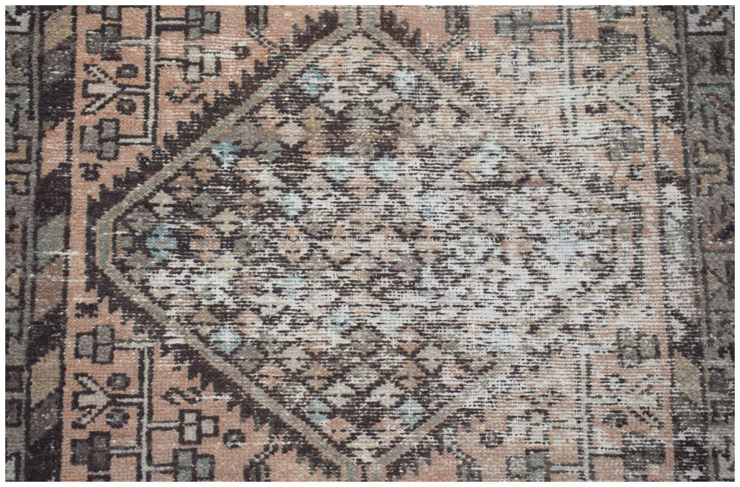A vintage handwoven Persian rug featuring a faded diamond medallion pattern in muted earth tones.