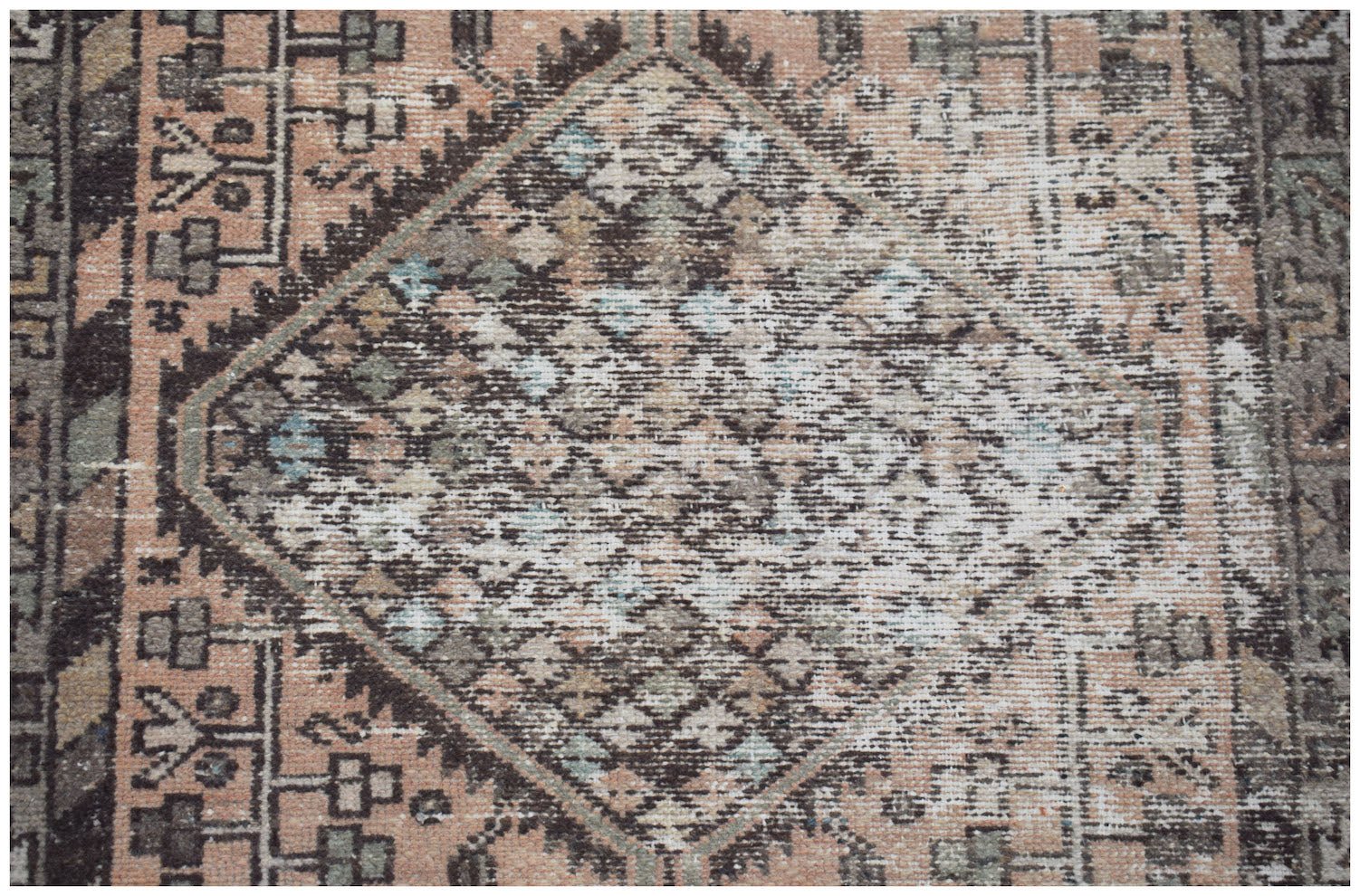 A vintage handwoven Persian rug featuring a faded diamond medallion pattern in muted earth tones.