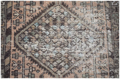 A vintage handwoven Persian rug featuring a faded diamond medallion pattern in muted earth tones.