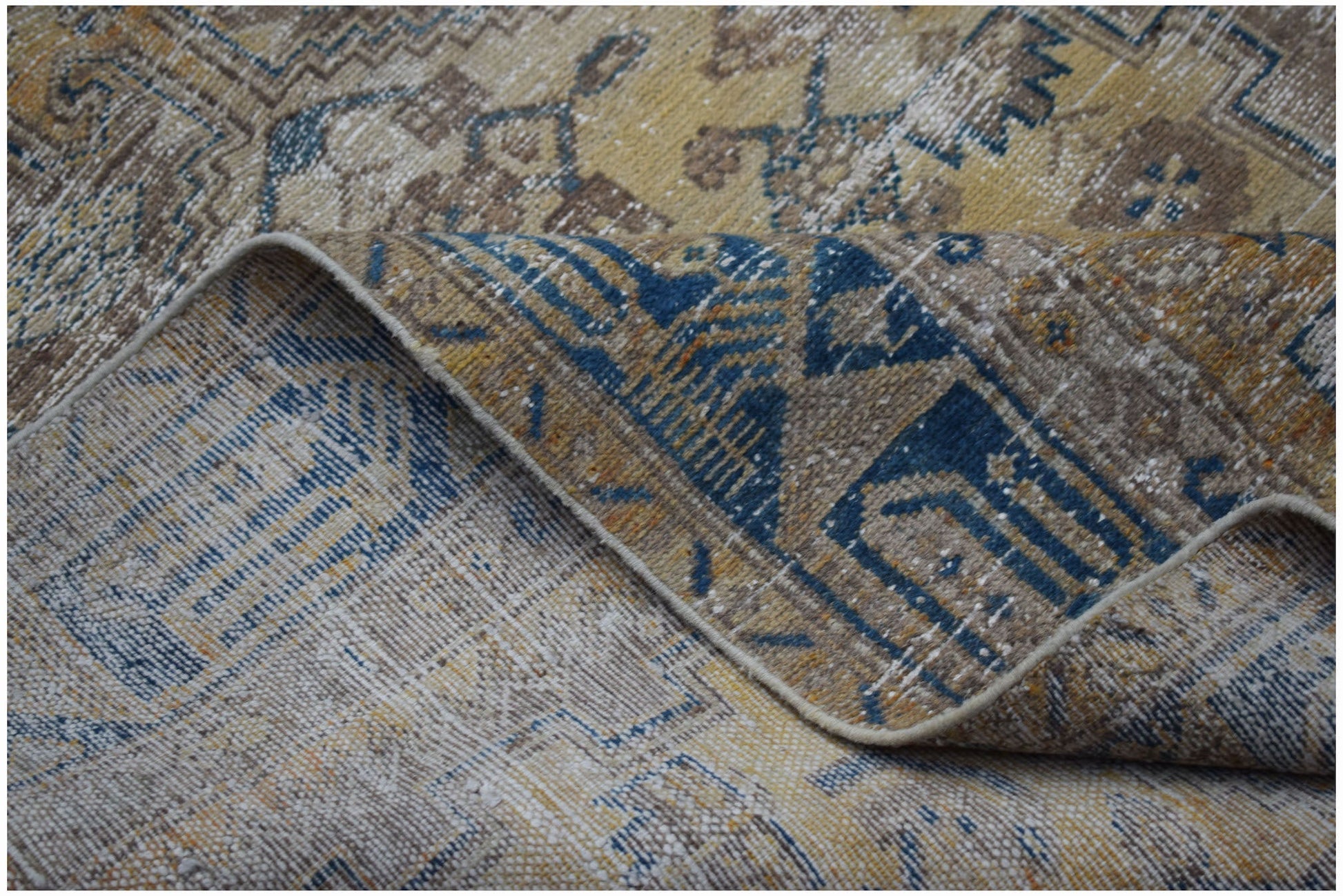 A folded vintage Persian rug featuring a distressed pattern in shades of blue, gold, and beige.