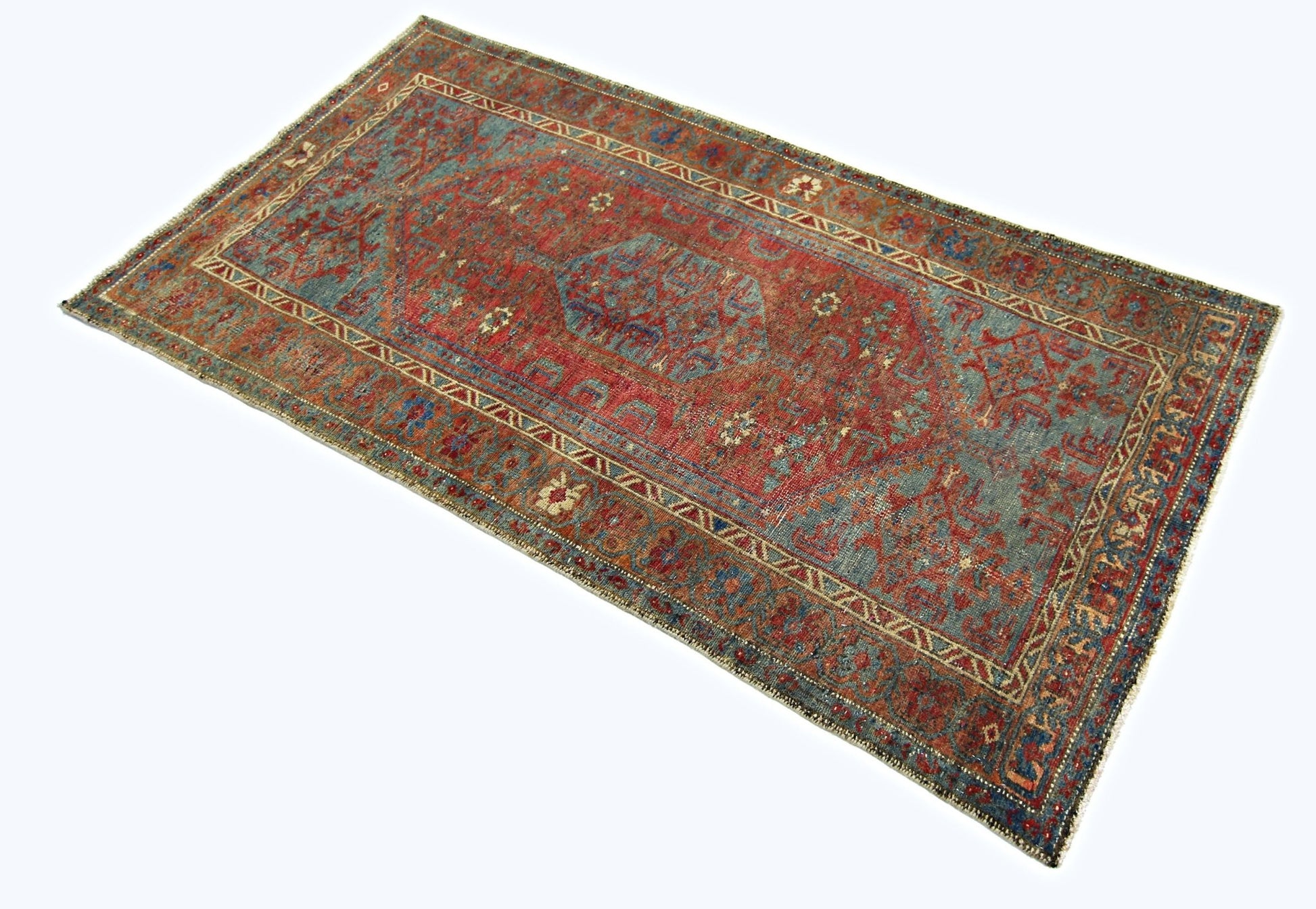 A rectangular vintage Persian rug featuring a red and blue geometric pattern on a white background.