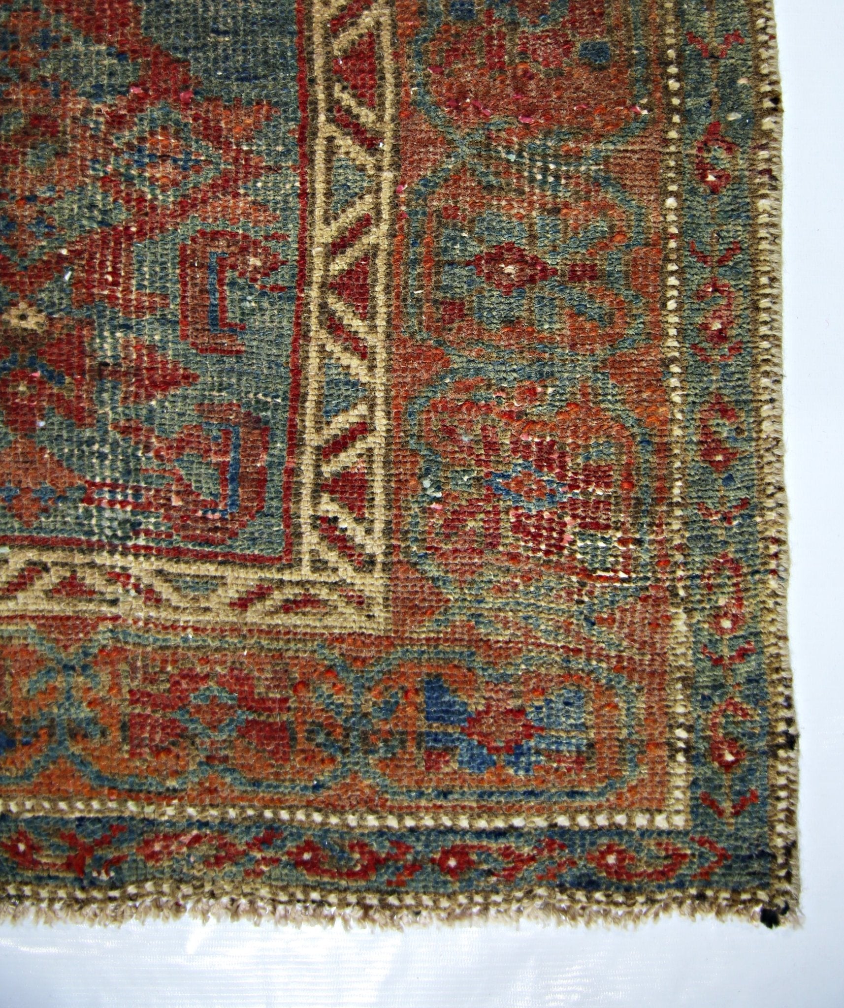 A close-up of a vintage handmade Persian rug featuring intricate geometric patterns in red and blue.
