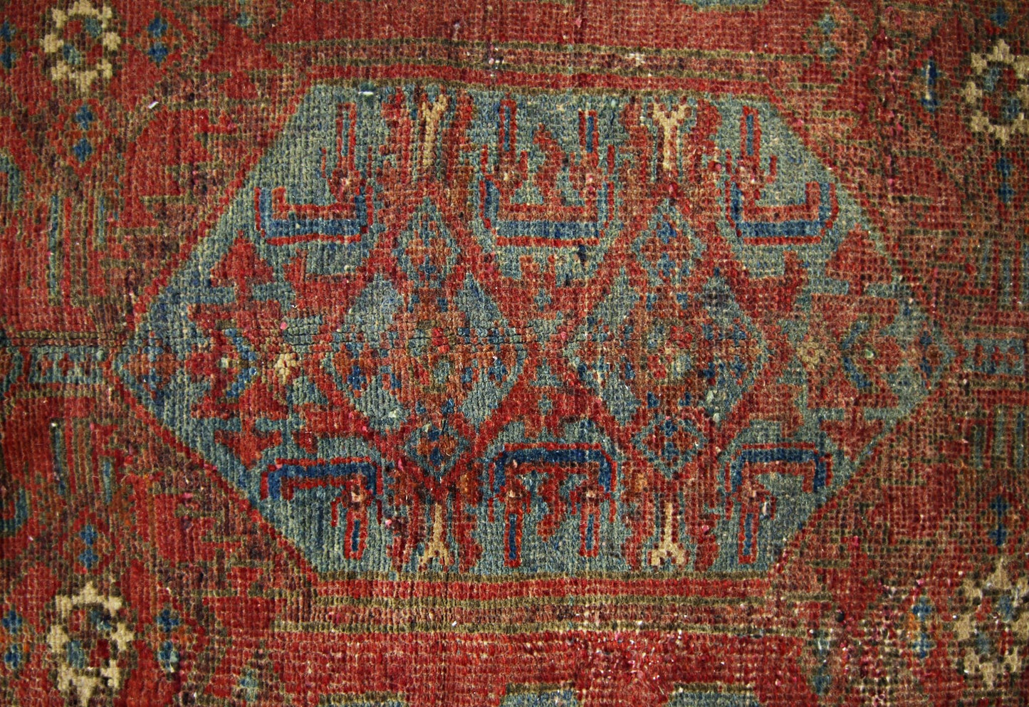 A vintage handmade Persian rug featuring a central blue geometric medallion on a red field.