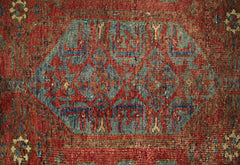 A vintage handmade Persian rug featuring a central blue geometric medallion on a red field.