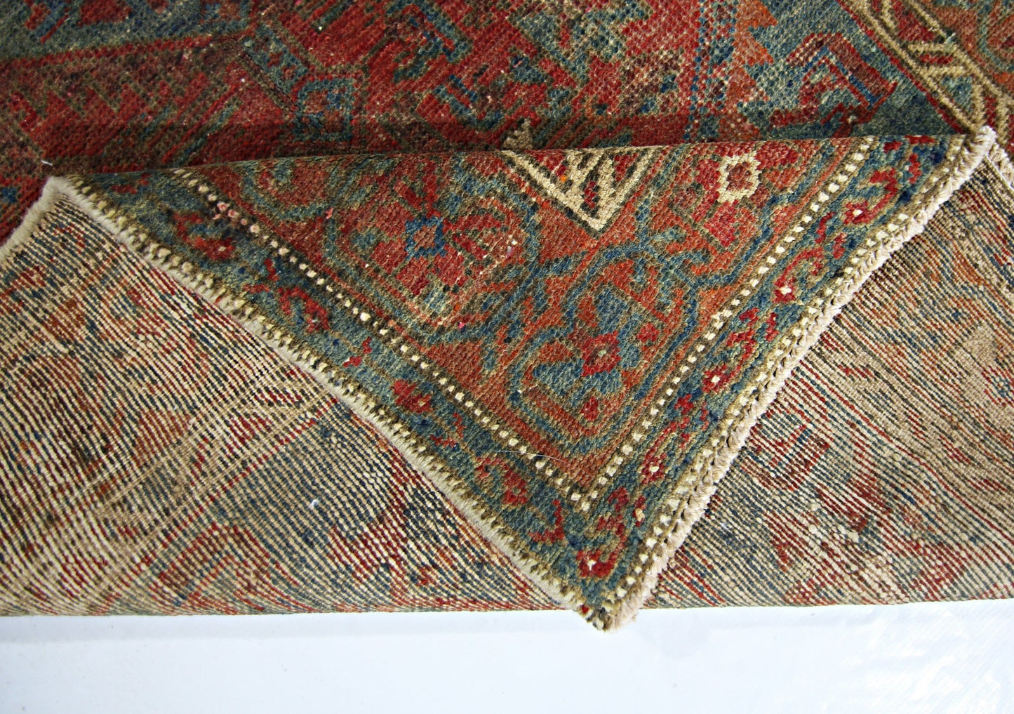 A vintage handmade Persian rug with a red and blue floral pattern, shown folded to reveal its weave.