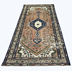 A vintage handmade Persian rug featuring a geometric medallion pattern in peach, blue, and cream.