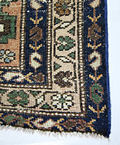 A close-up of a vintage Persian rug featuring intricate floral patterns in blue, tan, and green.