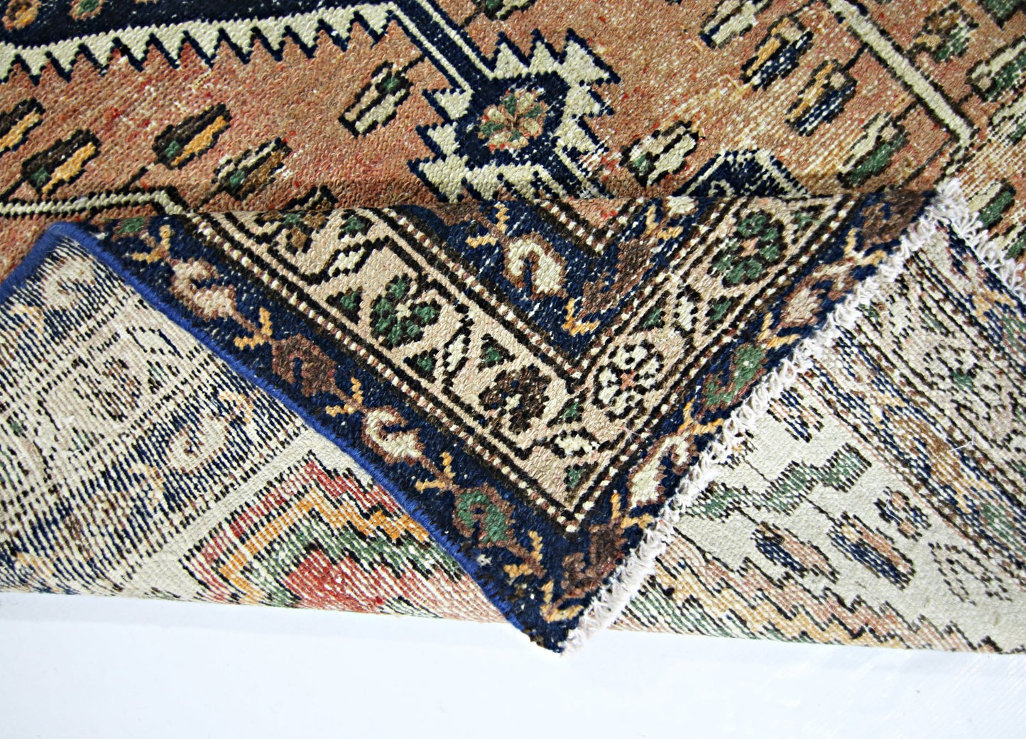 A folded vintage Persian rug featuring intricate geometric patterns in blue, tan, and green wool.