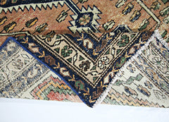 A folded vintage Persian rug featuring intricate geometric patterns in blue, tan, and green wool.