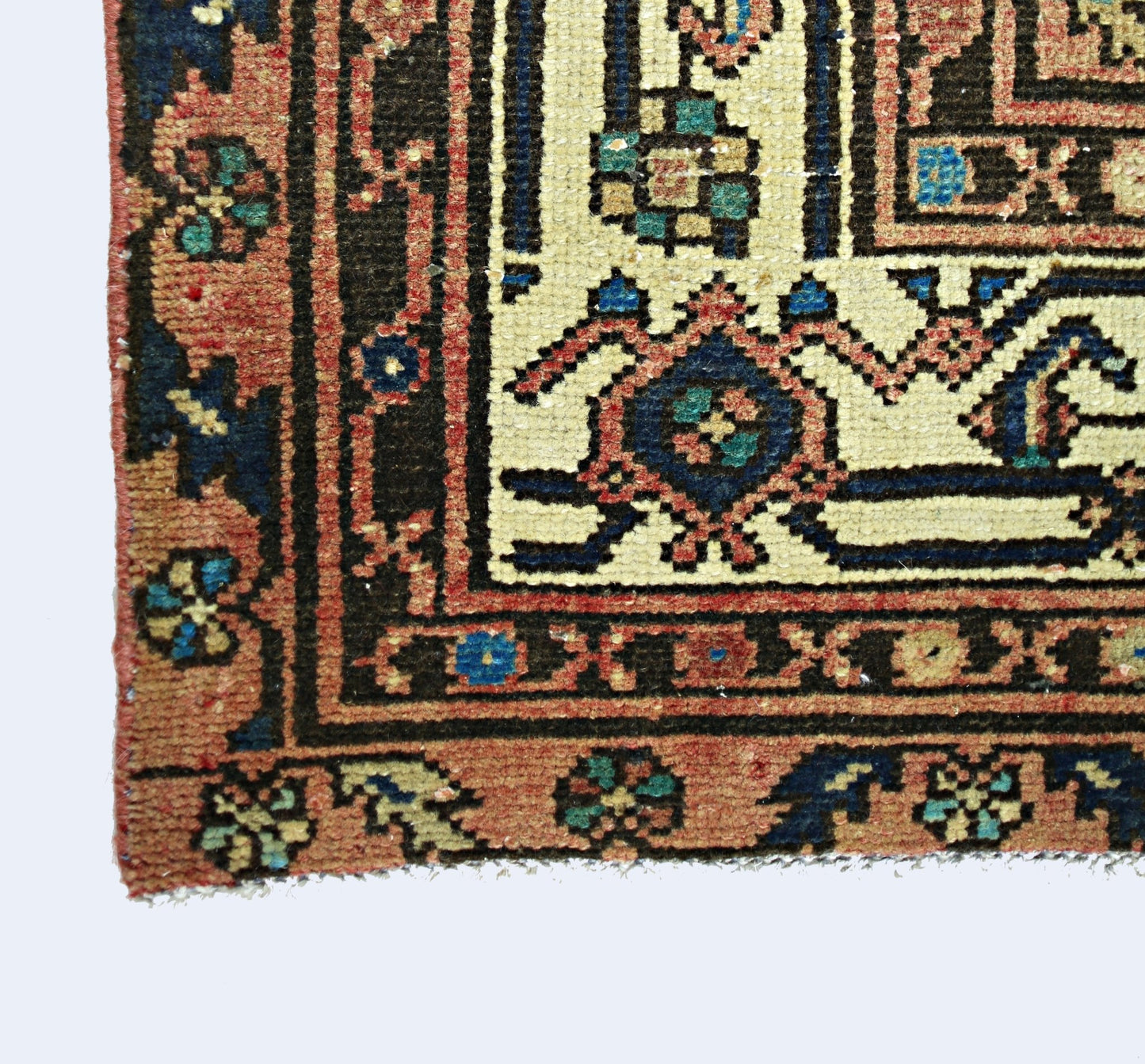 A corner view of a vintage Persian rug featuring intricate geometric patterns in red and blue.
