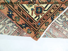 A folded vintage Persian rug featuring intricate geometric patterns in red, blue, and cream tones.