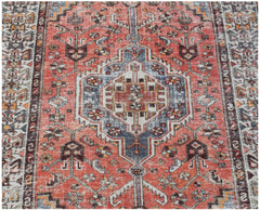 A vintage handwoven Persian rug featuring a central geometric medallion in red, blue, and cream.