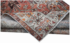 A folded vintage Persian rug featuring intricate geometric patterns in red, orange, and cream tones.