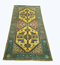 A handmade vintage Persian runner rug featuring geometric yellow medallions and teal borders.