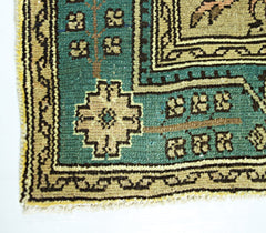 A close-up of a vintage Persian rug featuring a teal border with geometric floral patterns.