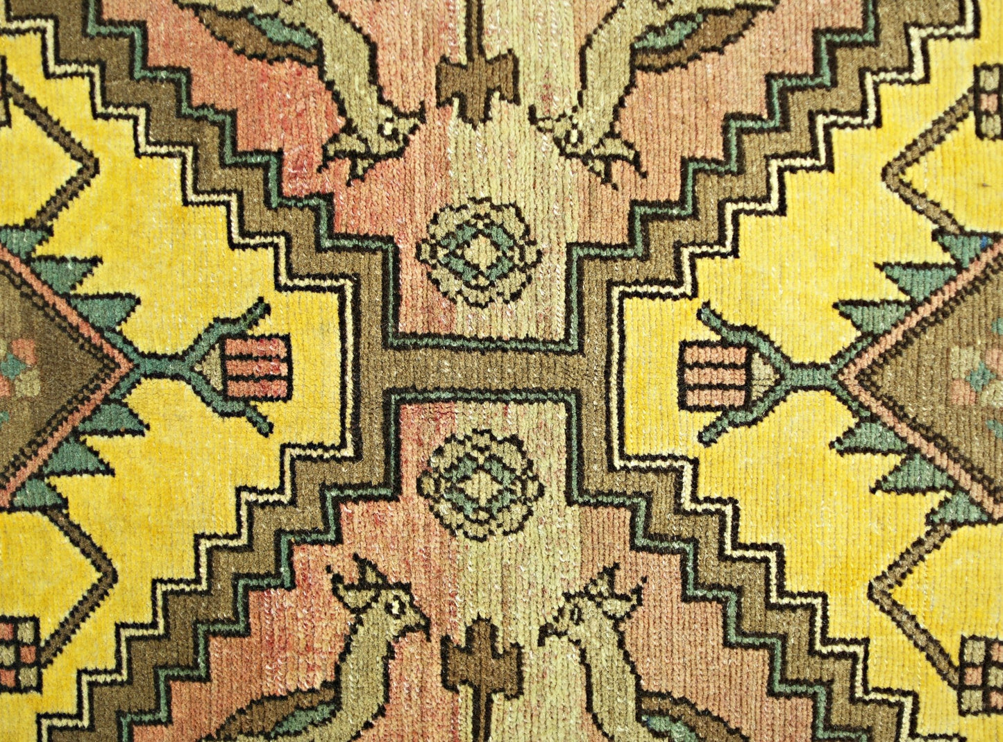 A close-up of a vintage Persian rug featuring geometric patterns in yellow, orange, and green.