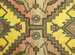 A close-up of a vintage Persian rug featuring geometric patterns in yellow, orange, and green.