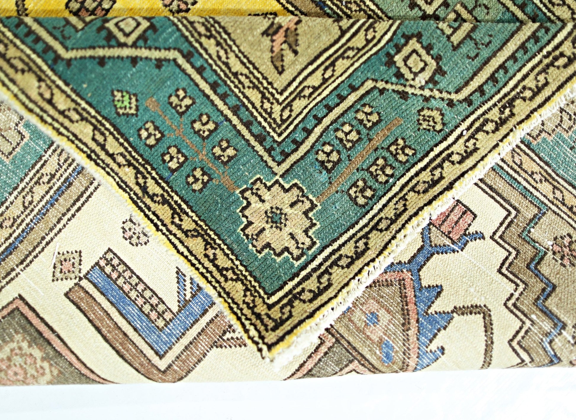 A folded vintage Persian rug featuring intricate geometric patterns in teal, beige, and blue.