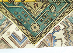 A folded vintage Persian rug featuring intricate geometric patterns in teal, beige, and blue.