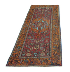 A vintage handmade Persian runner rug featuring a geometric floral pattern in red and orange tones.