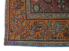 A corner view of a vintage Persian rug featuring intricate geometric patterns in orange and red.