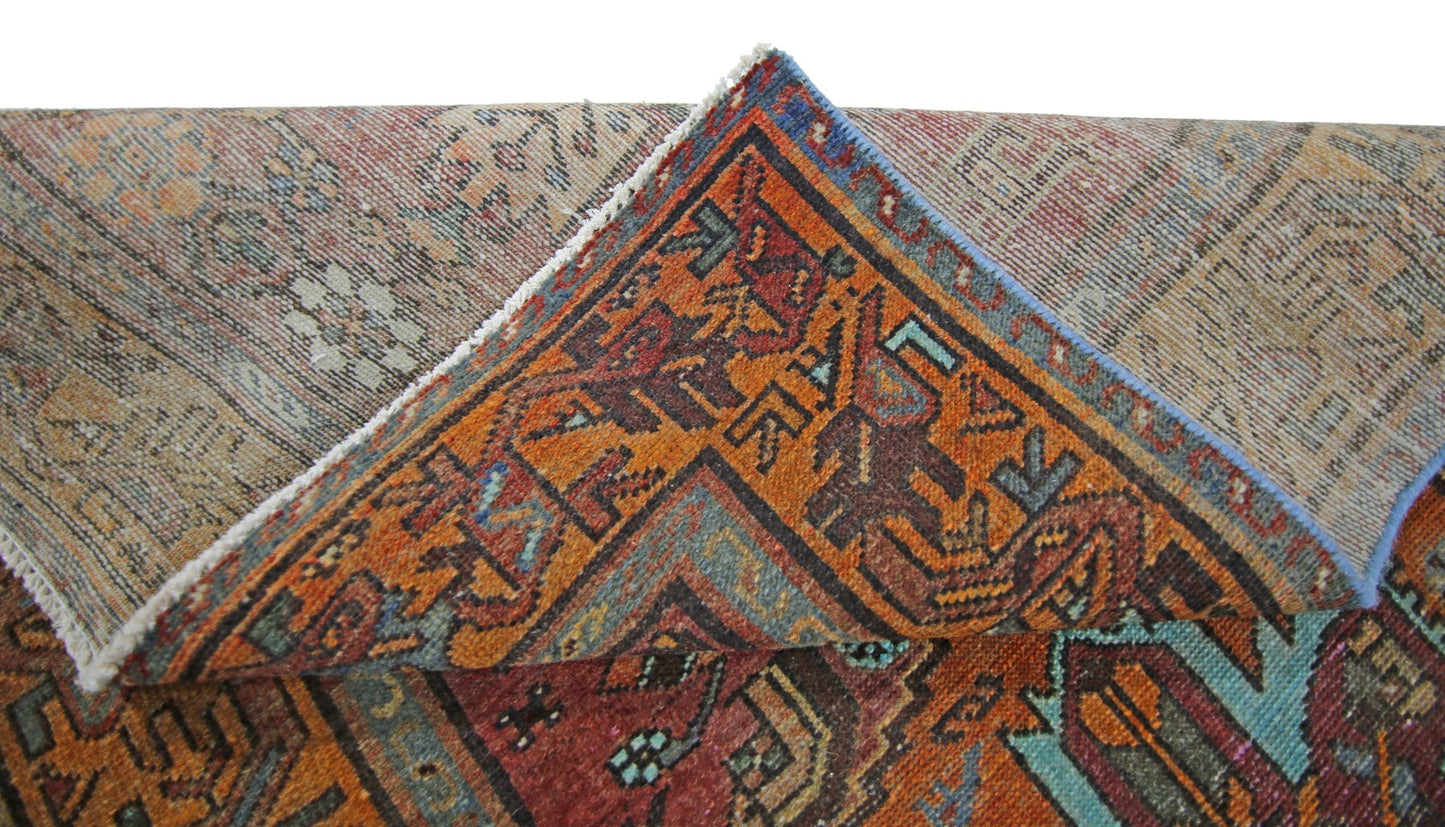 A folded vintage Persian rug featuring intricate geometric patterns in orange, blue, and red.