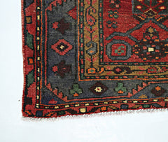 A corner view of a vintage Persian rug featuring geometric patterns in red, blue, and gold.