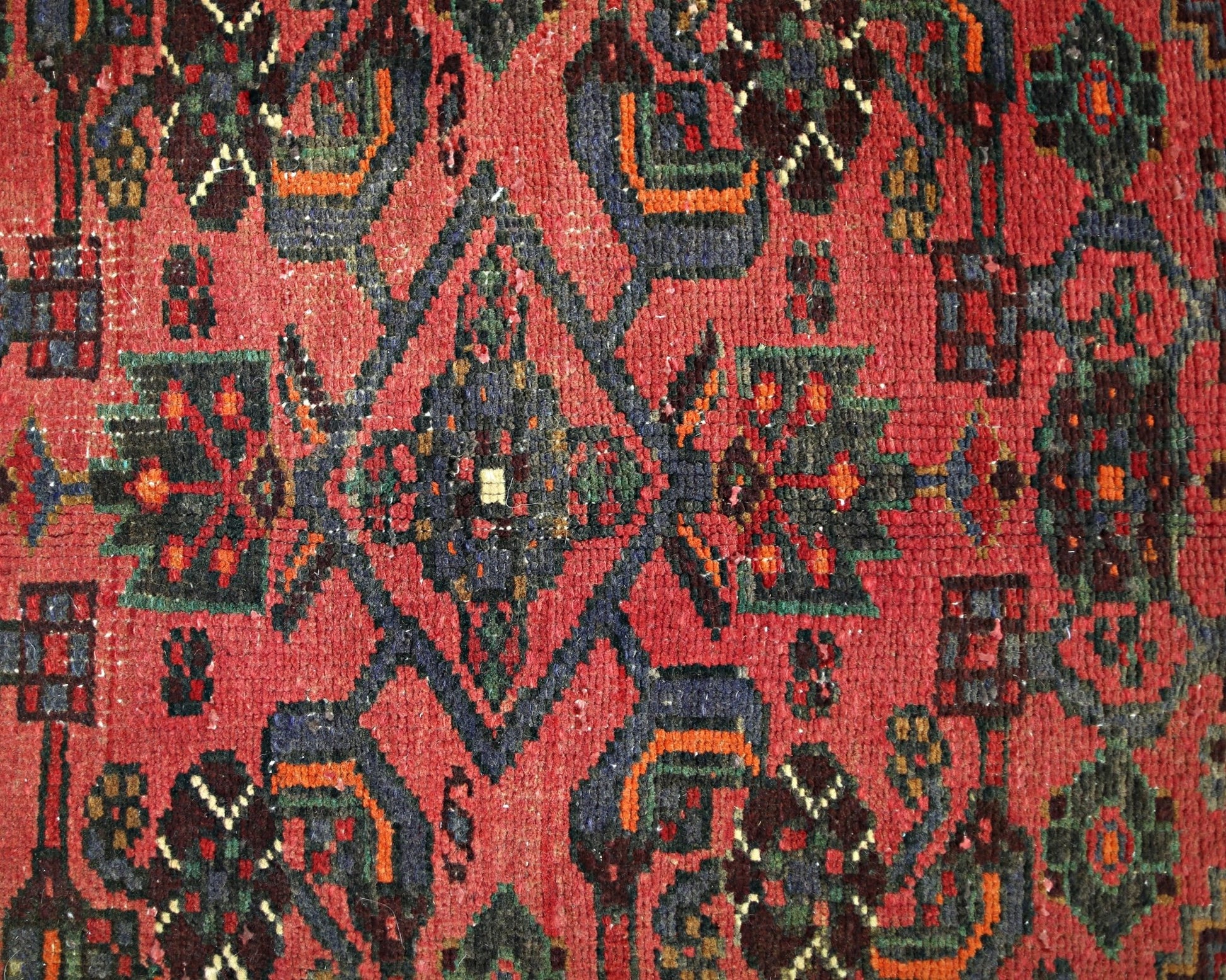 A vintage Persian rug featuring a geometric floral pattern in red, blue, and green tones.