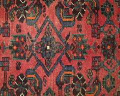 A vintage Persian rug featuring a geometric floral pattern in red, blue, and green tones.