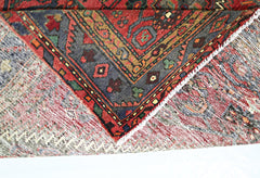 A corner of a vintage Persian rug folded over to show its intricate red and blue wool pattern.