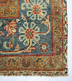 A vintage Persian rug featuring a blue field with floral patterns and a tan border.