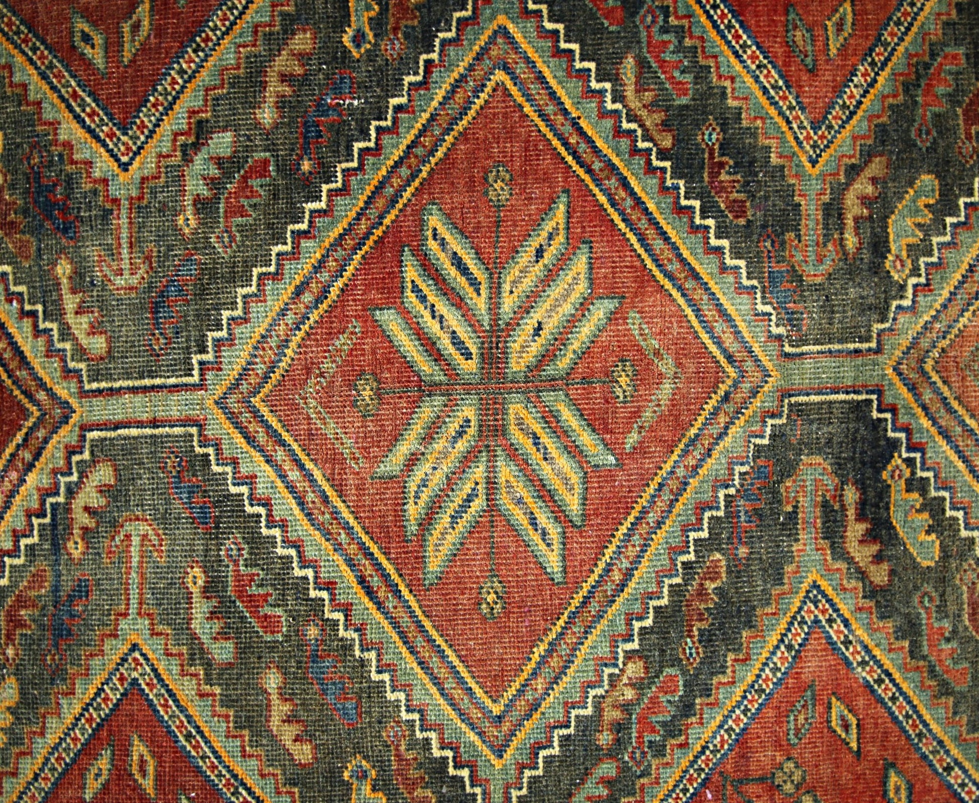 A vintage Persian rug featuring a geometric diamond pattern in red, blue, and yellow wool.