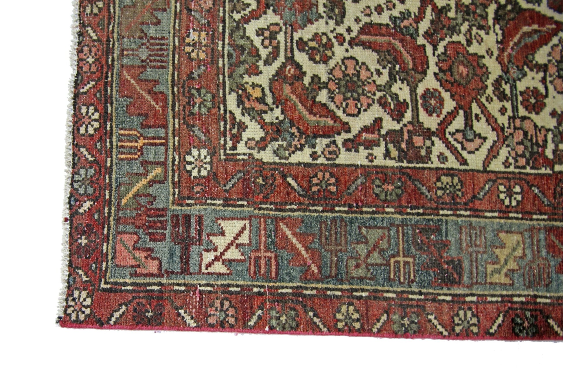 A corner view of a vintage Persian rug featuring intricate floral patterns in red, blue, and cream.