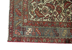 A corner view of a vintage Persian rug featuring intricate floral patterns in red, blue, and cream.