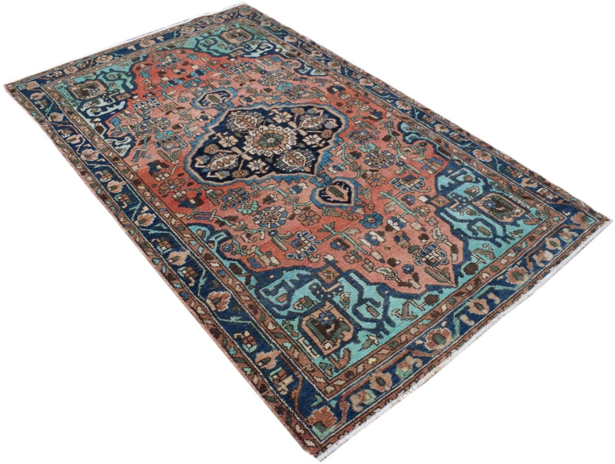A rectangular vintage Persian rug featuring a central medallion on a salmon and blue floral field.