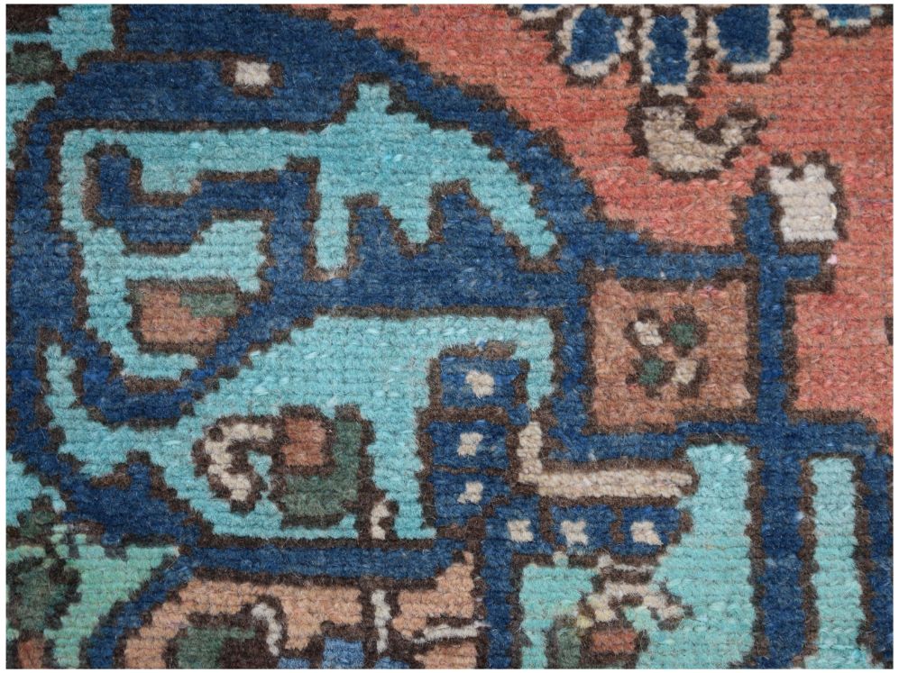 A close-up of a vintage Persian rug featuring intricate geometric patterns in blue and coral wool.