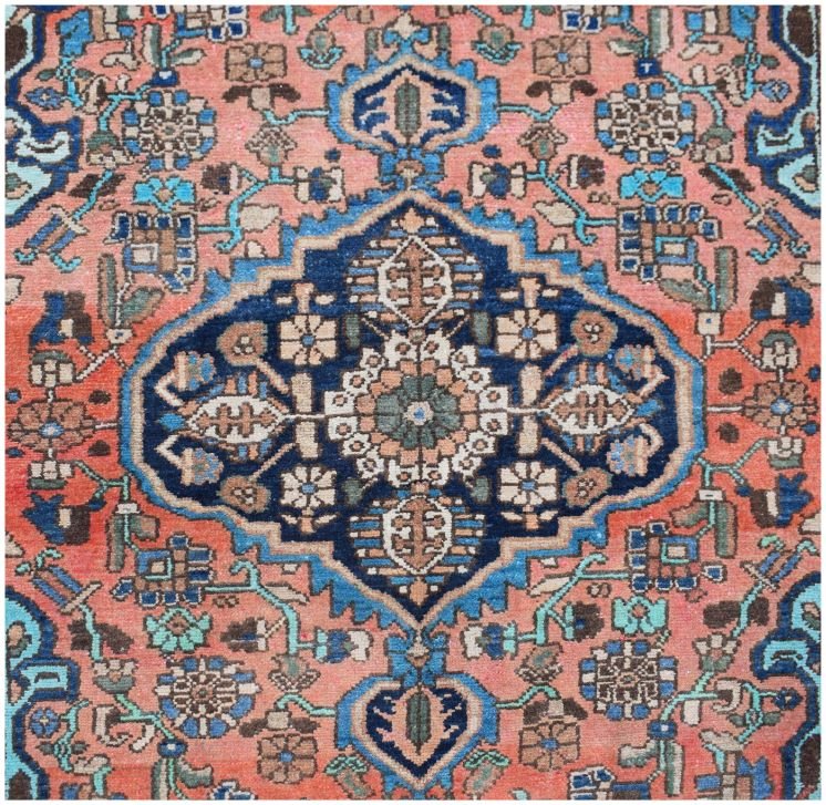 A vintage handmade Persian rug featuring a central blue medallion on a salmon pink background.