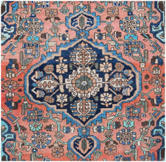 A vintage handmade Persian rug featuring a central blue medallion on a salmon pink background.